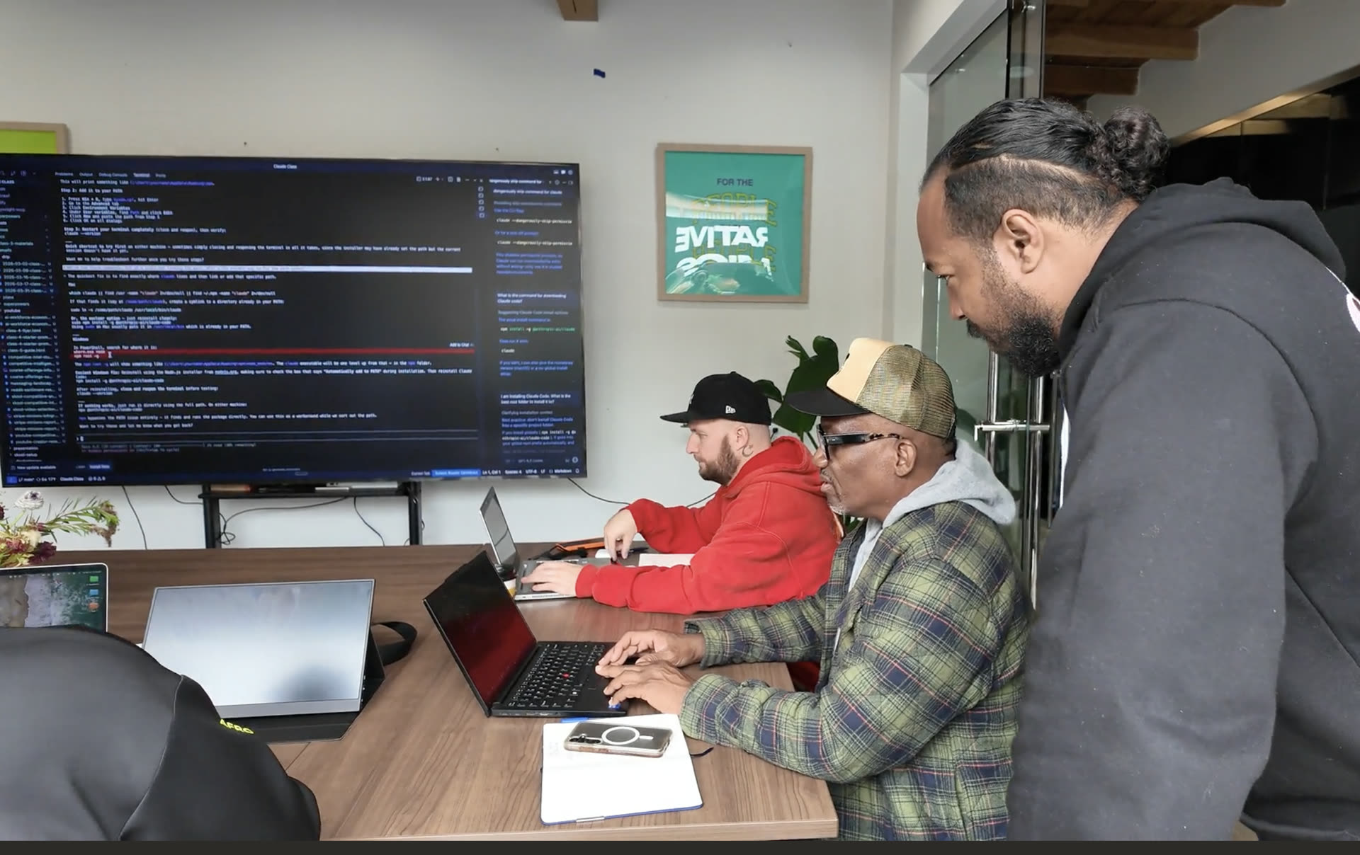 Workshop students building together at laptops with code on the screen behind them
